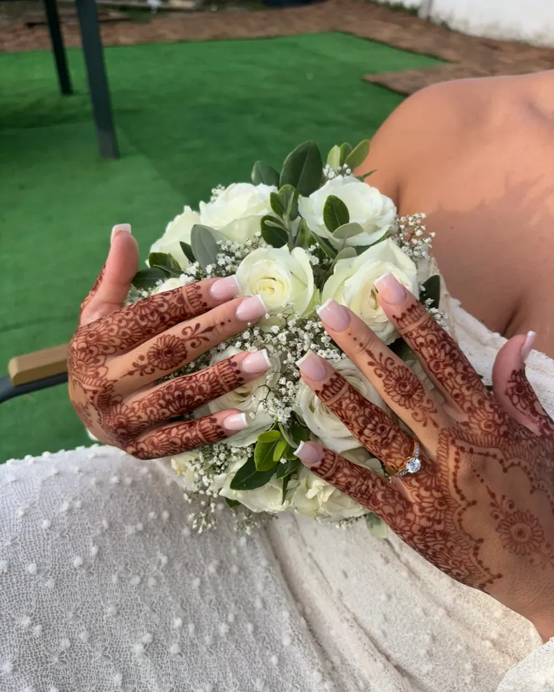 Mains aux motifs de henné posées sur un bouquet de roses blanches