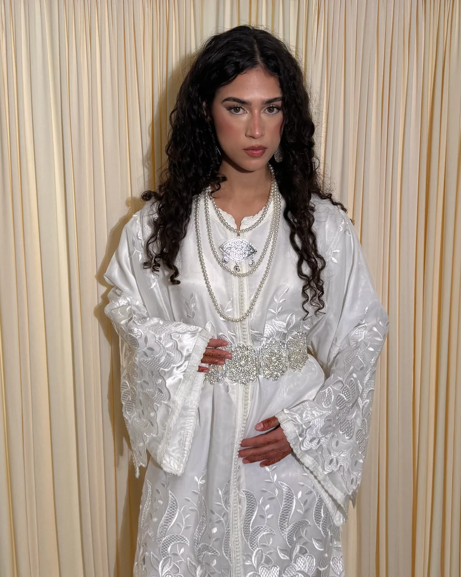 Caftan blanc brodé ton sur ton, porté avec colliers de perles et ceinture argentée